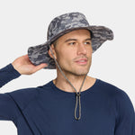 A man wearing a gray and black camouflage wide-brim sun hat with a chin strap, paired with a navy blue long-sleeve shirt, against a light gray background.