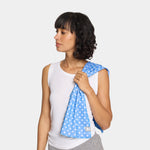A woman wearing a white tank top and gray sweatpants holds a light blue baby carrier with a white star pattern over her shoulder, shown against a light gray studio background.