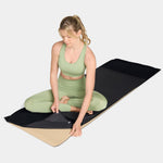 Woman in green athletic wear sitting on a black and beige Mission cooling yoga mat