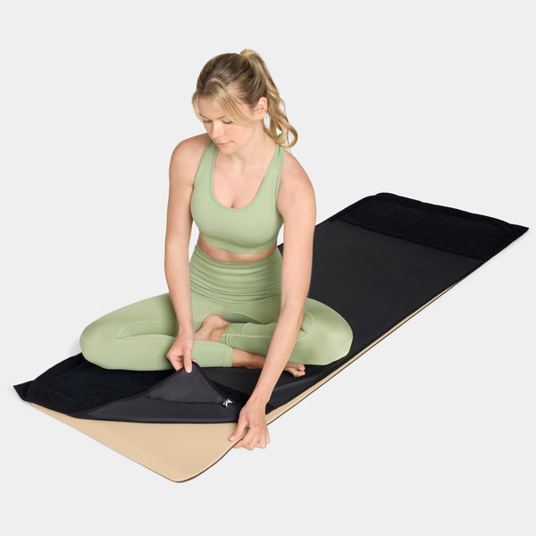 Woman in green athletic wear sitting on a black and beige Mission cooling yoga mat