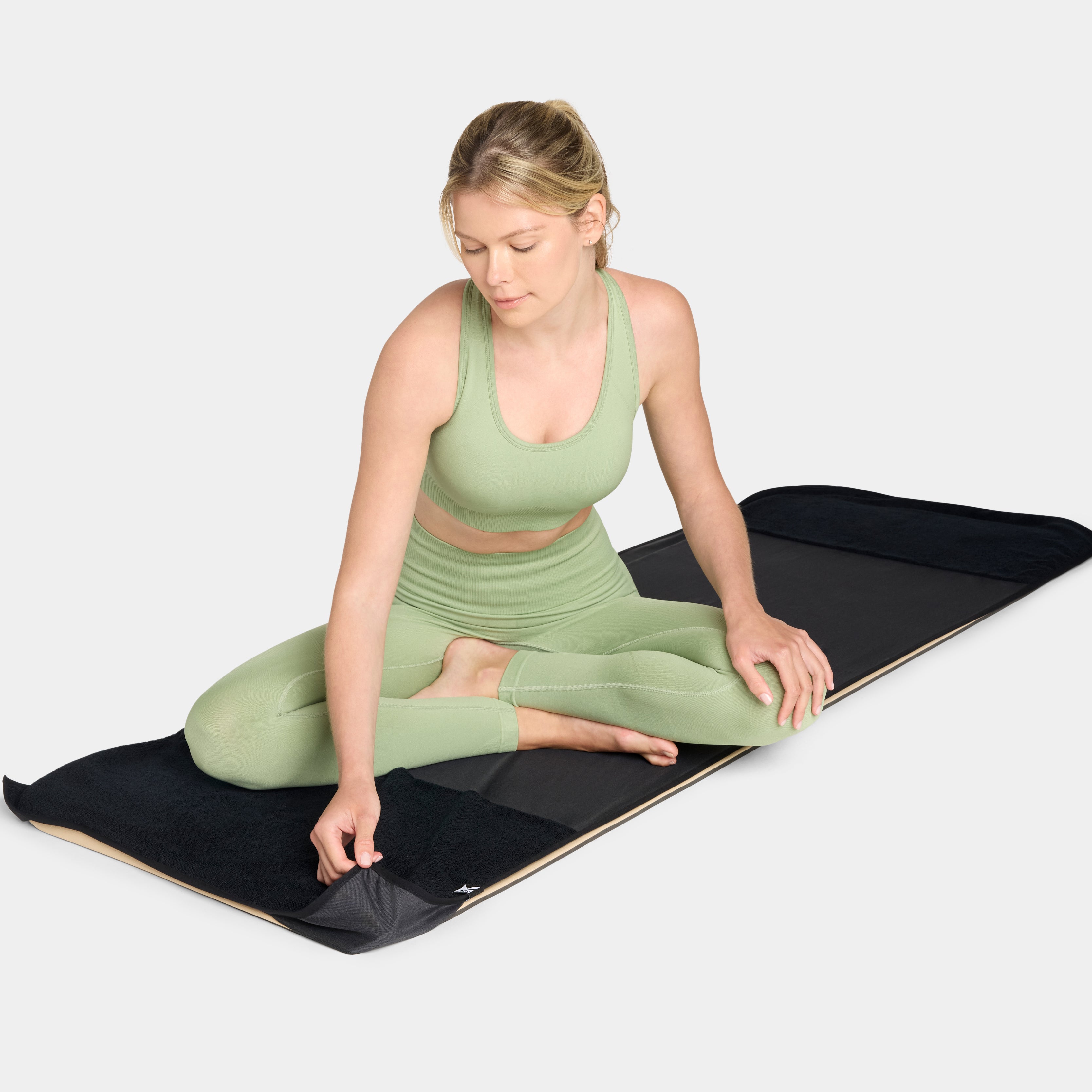 Woman in green athletic wear sitting on a black and beige Mission cooling yoga mat
