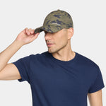 A man wearing a navy blue crewneck t-shirt and a green camouflage baseball cap with 'MEXICAN' embroidered on the front, posing against a light gray background.