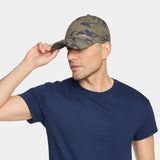 A man wearing a navy blue crewneck t-shirt and a green camouflage baseball cap with 'MEXICAN' embroidered on the front, posing against a light gray background.