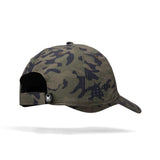A camouflage baseball cap shown from the back, featuring a green and black camo pattern, a black adjustable strap, and a small white circular logo patch on the side.