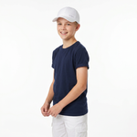A young boy wearing a navy blue crewneck t-shirt, a white baseball cap, and white cargo shorts, standing against a plain white studio background.