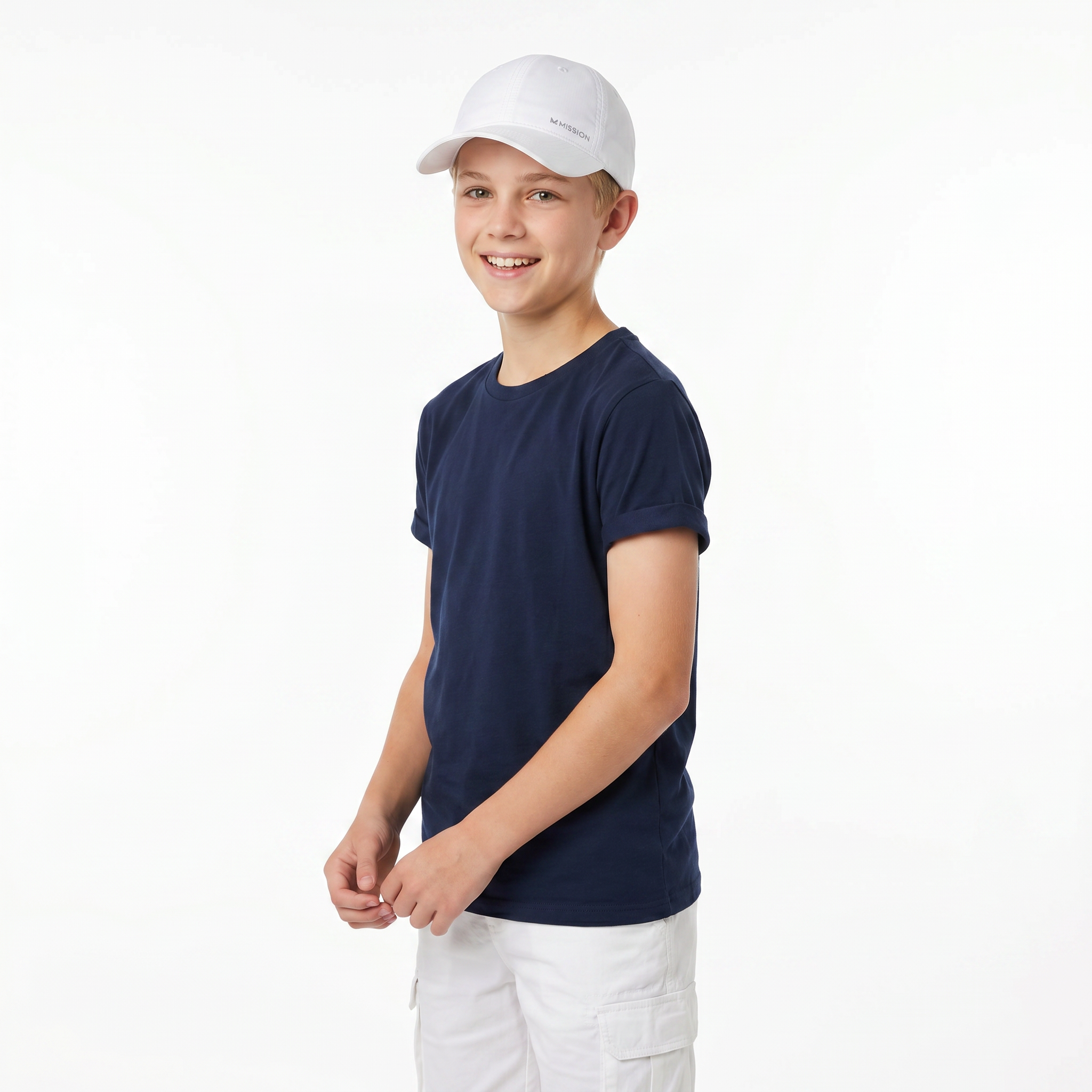 A young boy wearing a navy blue crewneck t-shirt, a white baseball cap, and white cargo shorts, standing against a plain white studio background.
